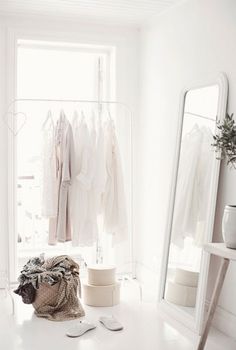 a white room with clothes hanging on the wall and a mirror in front of it