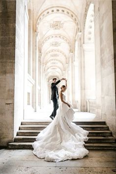 a bride and groom posing for a photo on the stairs in an old building with stone columns