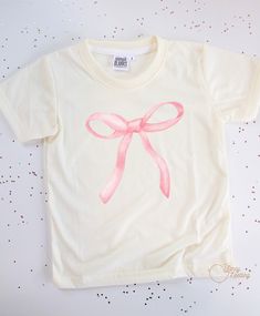 Our Pink Bow graphic tee is made with 100% polyester, ensuring durability and a comfortable fit. The cowboy design adds a fun and unique touch, making it perfect for any young adventurer. Upgrade their wardrobe with this high-quality tee today! *Don’t forget to choose your color tee: CREAM or WHITE *All tee brands run true to size. The graphic used on our tees are sublimation prints which means its printed into the fabrics on the shirt. No more peeling! *Care Instructions: Turn inside out & wash Cute Simple Shirt Designs, Cute Shirts Aesthetic Trendy, Making Graphic Tees, Bow T-shirt, Bow Tshirts, Pink Shirt Aesthetic, Pink Shirt Design, Coquette Wishlist, Mini Tees