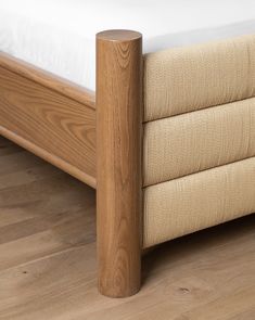 a wooden bed frame with white sheets and wood flooring