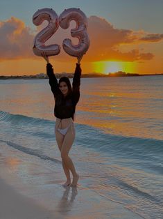 a woman is standing on the beach with her arms in the air while holding two large balloons