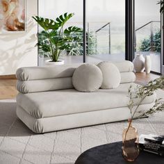 a living room filled with lots of furniture and plants on top of the tables in front of large windows