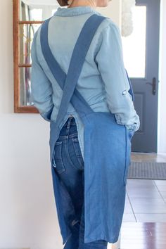 the back of a woman wearing overalls and a blue shirt is standing in front of a mirror