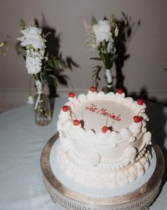 there is a wedding cake on the table with flowers in the vases behind it