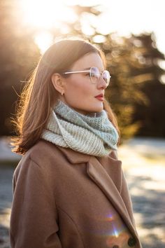 a woman wearing glasses and a scarf standing in the sun with her hands on her hips