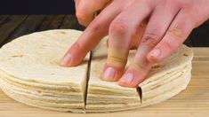 a person cutting into tortillas on top of a wooden table with a knife