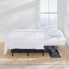 a bed sitting in front of a window next to a rug on top of a floor