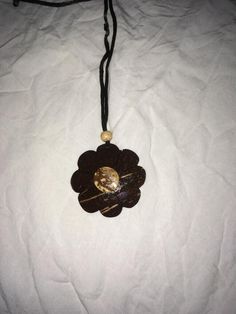 a necklace with a flower on it is laying on a white sheet and has a black cord