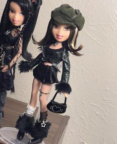 two dolls are standing next to each other holding purses and shoes on a table