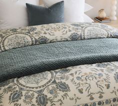 a bed with blue and white comforter on top of it next to a night stand