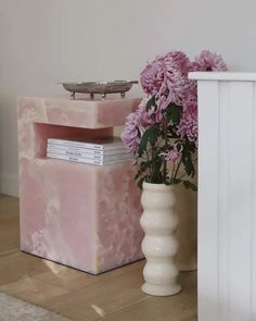 a vase with flowers sitting next to a pink marbled box on the floor in front of a white radiator