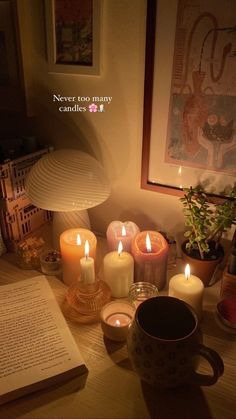 lit candles and books on a table in front of a wall with an open book