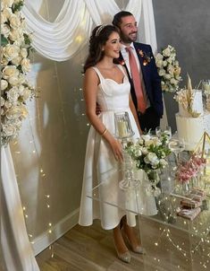 a man and woman standing next to each other in front of a table with flowers