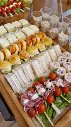 an assortment of sandwiches and salads on a wooden platter at a buffet table