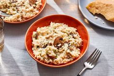 two orange bowls filled with rice and mushrooms next to silverware on a white tablecloth