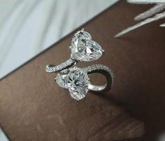 two heart shaped diamond rings sitting on top of a brown book next to an ornament