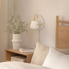 a bed with white sheets and pillows next to a table with a lamp on it