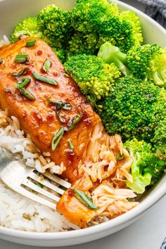 a white bowl filled with rice, broccoli and salmon next to a fork