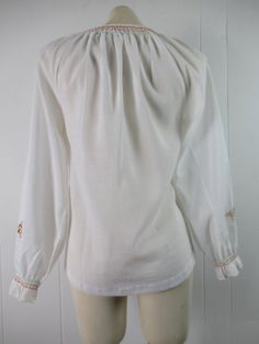 "Vintage 1970s peasant shirt ethnic blouse. Made of white poly/cotton. Has bohemian embroidery on front and arms. Tie at the neck. Made by Lily. About a size small/medium. Actual measurements are: 36\" at the bust 38\" at the waist 16\" shoulder to shoulder 22\" shoulder to end of sleeve 24.5\" overall length In very good condition." White Peasant Top With Boho Collar, White Boho Collar Peasant Top, Traditional White Peasant Top For Fall, Spring Peasant Top With Yoke Detail, Spring Peasant Top With Yoke, Peasant Style Long Sleeve Embroidered Top, Spring Folk Blouse With Yoke, Fall Peasant Blouse With Floral Embroidery, White Cotton Hippie Blouse