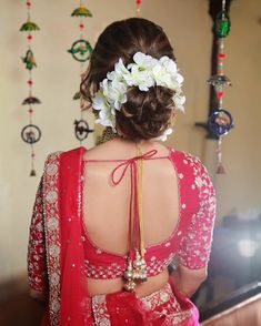 the back of a woman wearing a red sari with flowers in her hair and jewelry