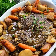 a white bowl filled with meat, potatoes and carrots next to parsley on top of a wooden table