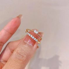 a woman's hand holding a gold ring with two diamonds on top of it