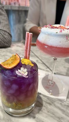 two cocktails sitting on top of a table next to each other with orange slices