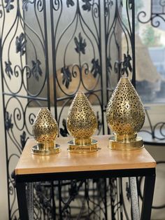 three gold vases sitting on top of a wooden table next to a black iron fence