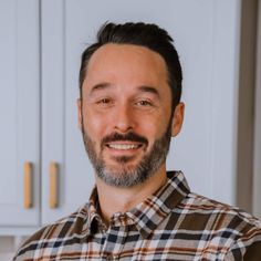 a man with a beard standing in front of white cupboards and smiling at the camera