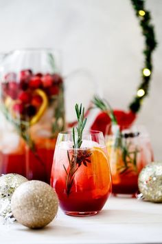 three glasses filled with different types of drinks next to christmas decorations and baubles