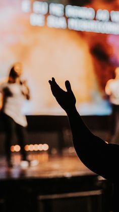 a person standing in front of a large screen with their hands up to the sky