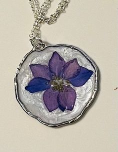 a purple flower is in the center of a silver circle pendant on a white surface