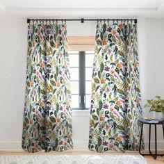 the curtains are hanging in front of the window with floral designs on them, along with a rug and side table