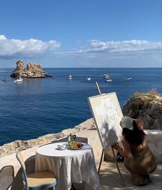 a person sitting at a table with an easel in front of the ocean