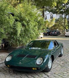 a green sports car parked in front of a tree on a cobblestone street