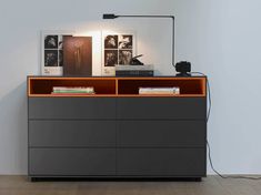 a modern dresser with books and pictures on the top, along with a lamp above it