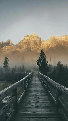 a wooden bridge with mountains in the background on a foggy day at sunrise or dawn