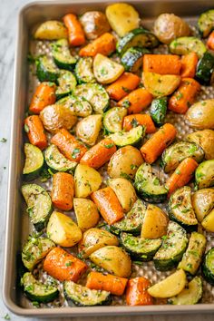 roasted vegetables in a baking pan with herbs on top, including carrots and zucchini