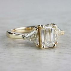 a three stone diamond ring on a white surface with gold trim around the band and sidestones