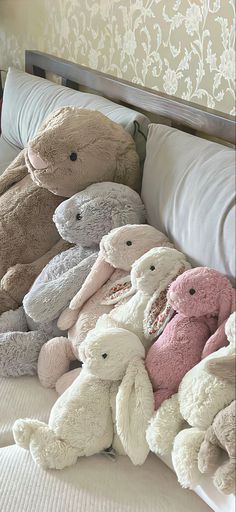 many stuffed animals are laying on a bed with white linens and pillows in front of the headboard