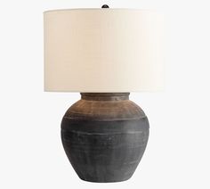 a black vase with a white shade on it's side and a light in the middle