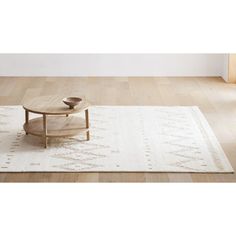 a coffee table on top of a rug in front of a white wall and wooden floor