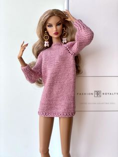 a barbie doll wearing a pink knitted sweater and matching heels, leaning against a wall