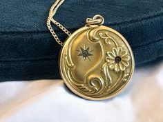 Description: Lovely antique Art Nouveau gold filled photo locket on a 14K gold filled chain. The front features an ornate repousse design with flowers and some leafy and curling designs on the bottom edge and two round faceted paste (glass) gems. The locket hangs on a new 14K gold filled curb chain with a spring ring clasp.  On the locket front top left section is an etched starburst shape that has a clear paste gem set inside it. On the right bottom side is a raised ten-petaled flower with a wonderful Repousse curled stem. The flower is set with a pink paste gem in the center. The flower and its stem along with some other decorative swirls fill up and curl around the bottom of the locket and create a lovely contrast to the starburst on a satin background on the opposite / top left side. Gold Medallion Locket Necklace Stamped 14k, Gold Heirloom Brass Locket Necklace, Heirloom Gold Brass Locket Necklace, Victorian Gold Locket Necklace With Vintage Charm, Antique Medallion Locket Necklace Stamped 14k, Ornate Gold Brass Locket Necklace, Victorian Round Locket Necklace Stamped 14k, Ornate Gold Locket Necklace In Brass, Anniversary Filigree Yellow Gold Locket Necklace