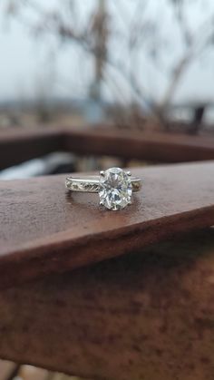 an engagement ring sitting on top of a wooden table next to a tree in the background