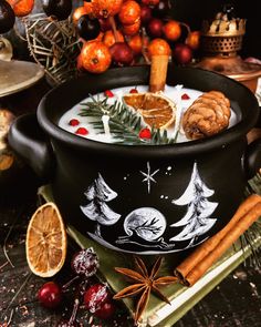 a black pot filled with food next to oranges and cinnamons on top of a table