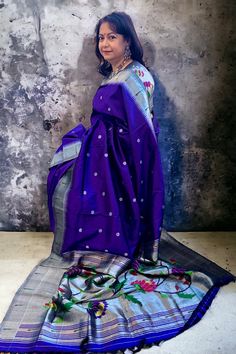 This exquisite regal paithani saree is handwoven in bluish purple color. Silver zari dollar buttis adorn the body while the silver zari border is decorated with handwoven in muniya border. The elaborate pallu is woven with colorful lotus along with winding vines. The saree comes with plain blouse with matching borders. Approximate Length 6.5 mtrs (inclusive of blouse length)Height - 48- 52" Saree comes with fall, picot and tassels done. Blouse piece is cut. Approximate weight - 1.8 lbs Kindly Note : The colors you see on your device may vary due to the color reproduction, brightness and resolution of individual devices. If you'd like more clarity before your purchase, please contact our support team. Plain Blouse, Silk Cotton Sarees, Blouse Length, Blouse Piece, Cotton Saree, Purple Color, Silk Sarees, Tassels, Hand Weaving