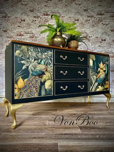 an ornate dresser with peacocks painted on it's drawers and gold handles, sits in front of a brick wall