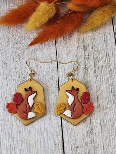 a pair of earrings with an image of a fox and acorns on it