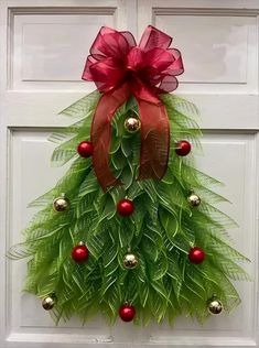 a christmas wreath on the front door with red balls and green leaves hanging from it